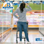 Image of woman with a shopping cart, from behind, with her arm near her head, appearing sad or frustrated in a grocery store aisle.