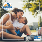 Image of Caucasian mother and young son, sitting on the ground outside embracing, next to some water bottles and a basketball.