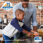 Image of an African American father and young son washing carrots in a kitchen sink.