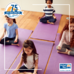 Image of four diverse children, meditating with their eyes closed on purple yoga mats.